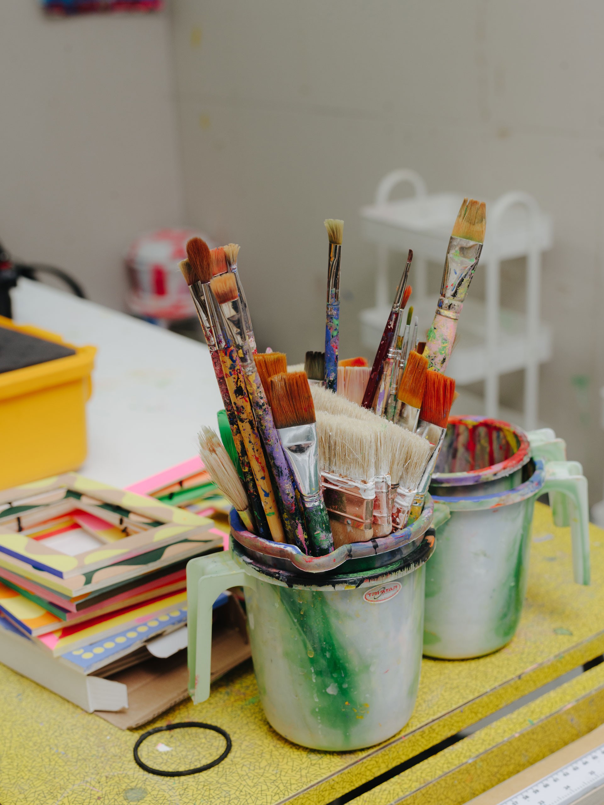 Alt-Tag: Two close-ups in Lakwena’s studio. One shows her creating a sketch, the other shows painting utensils.